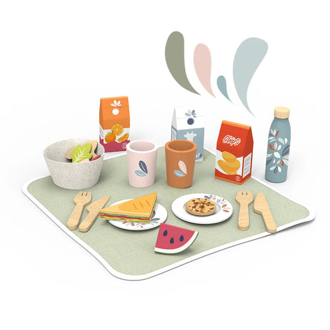 Open picnic basket with patterned lid, cups and snacks on green play mat