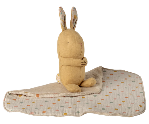 Seated yellow bunny with long ears beside its cream polka dot blanket