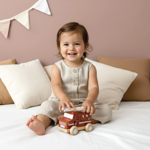 Baby playing with brown fire truck toy with white wheels on bed